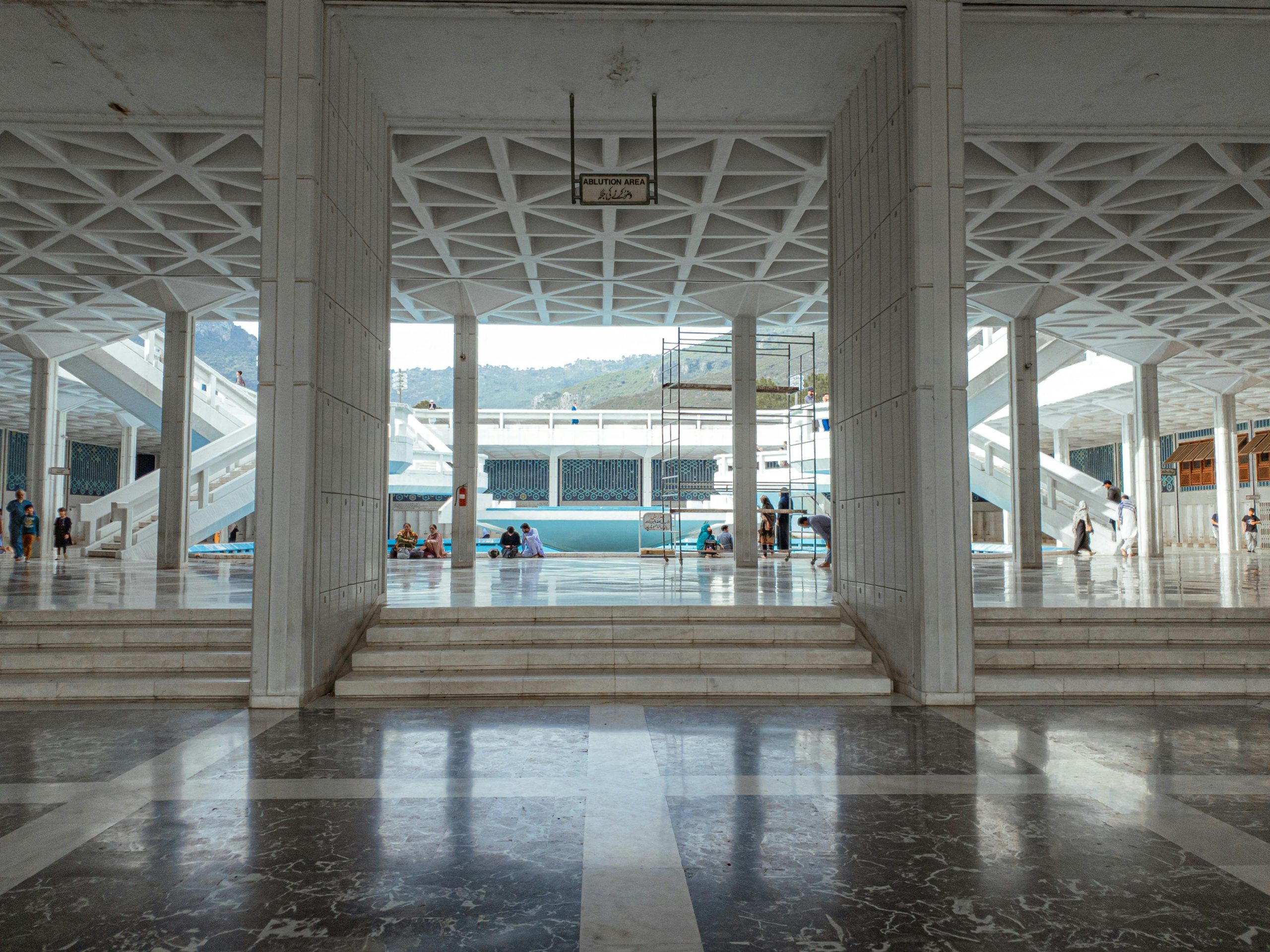 Home Wide view of Shah Faisal Mosque with people in the courtyard under geometric ceilings.