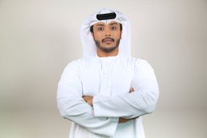 Home Young Middle Eastern man in white thobe standing confidently indoors.